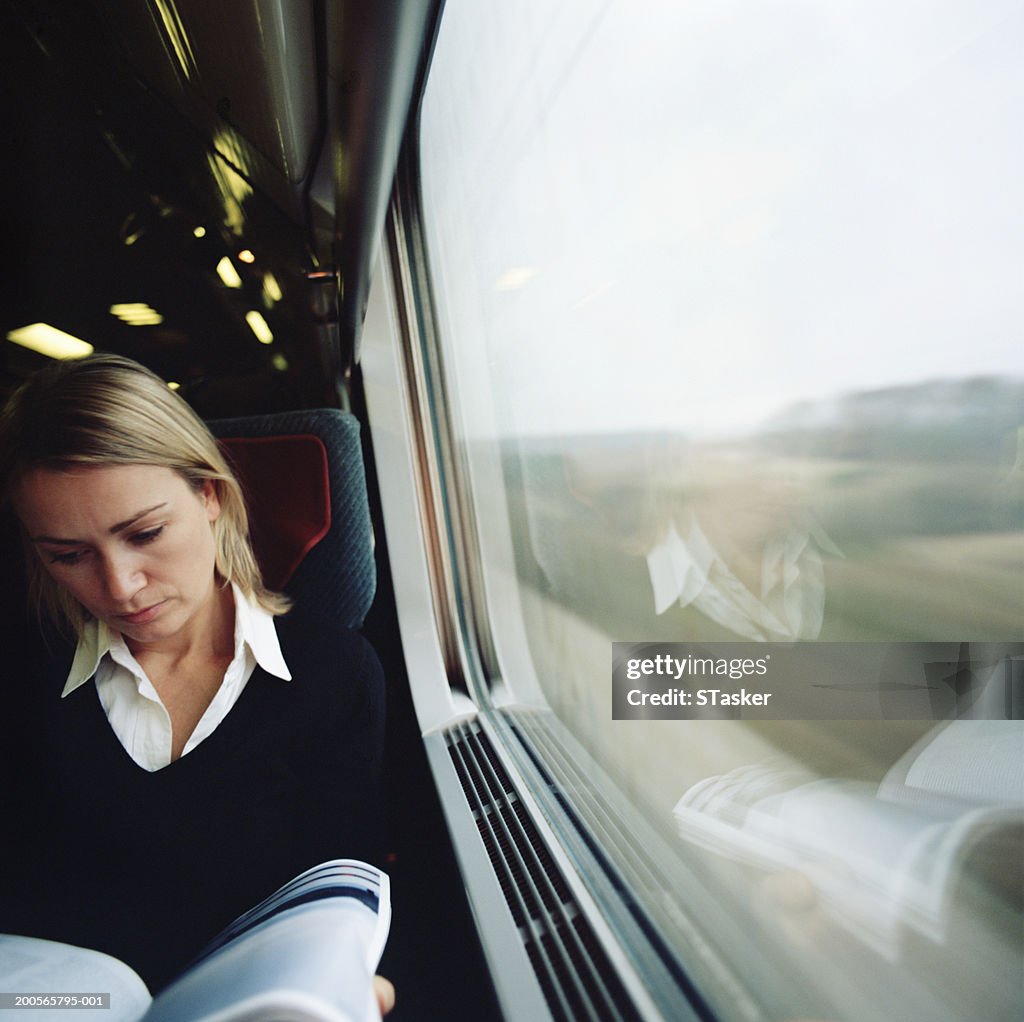 Woman sitting in train, reading magazine