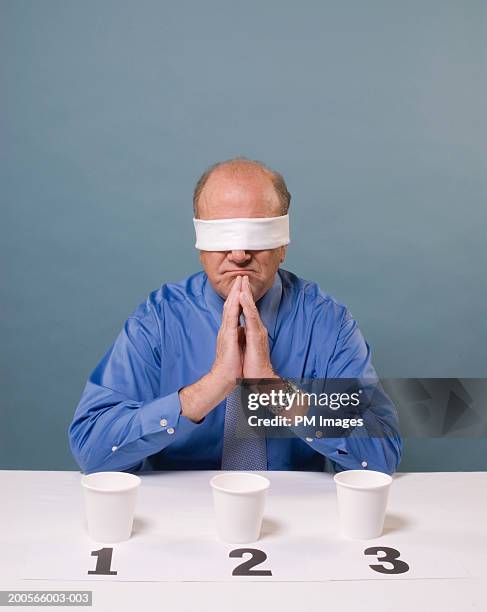 middle aged man taking taste test, blind folded, sitting with hands clasped - taste test stock pictures, royalty-free photos & images