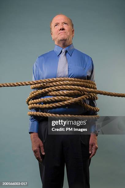 mature businessman wrapped in rope, three quarter length - gebunden stock-fotos und bilder