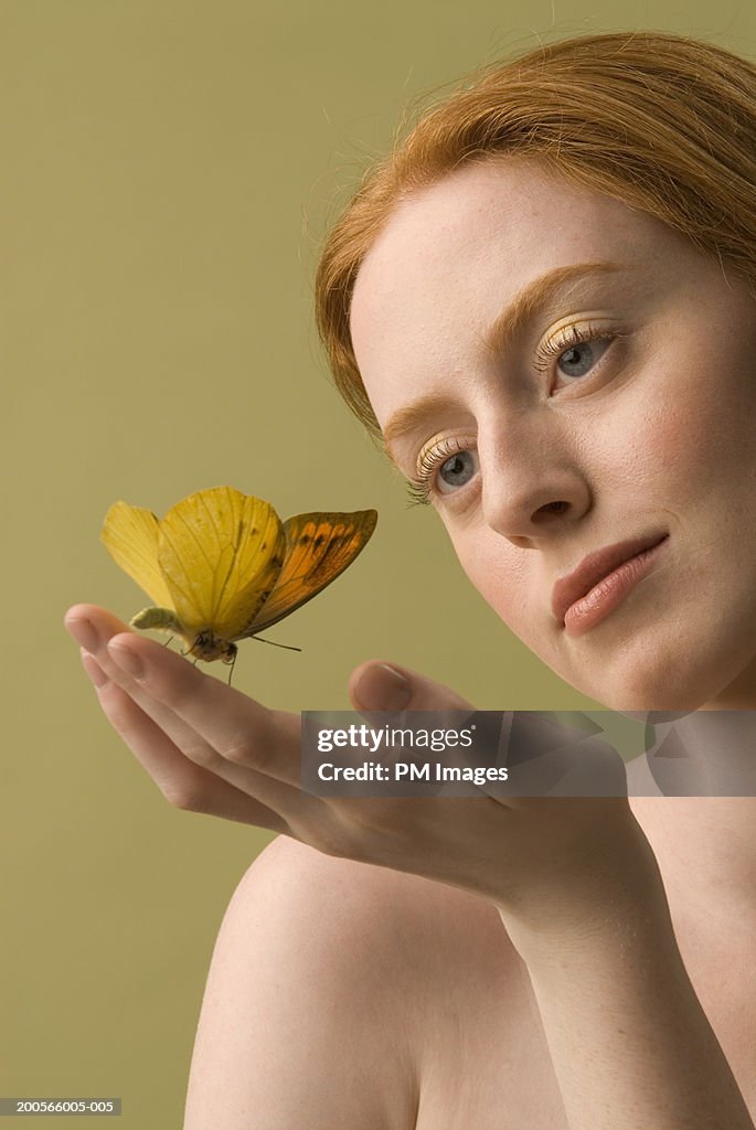 Young woman with ginger hair, looking at butterfly sitting on hand