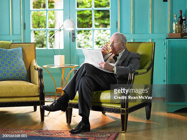 senior man sitting in armchair reading newspaper - newspaper luxury stock-fotos und bilder