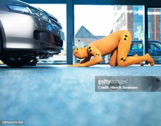 man dressed as crash test dummy inspecting bottom of new car, ground view - crash test dummies stock-fotos und bilder