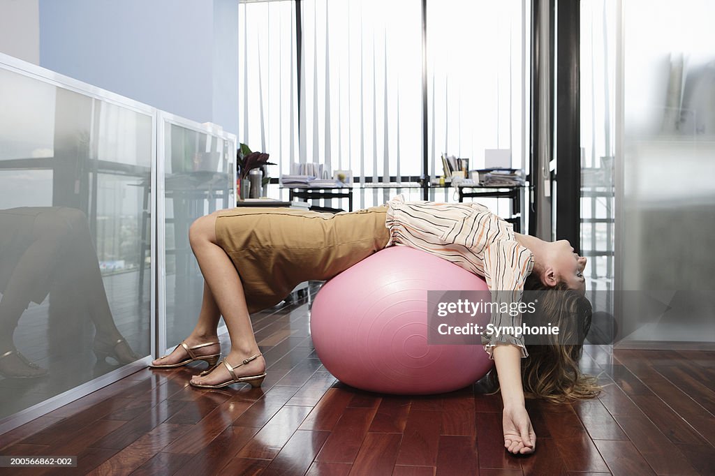 Business woman lying on exercise ball in office