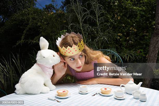 girl (10-11) wearing crown having tea party with toy rabbit - märchen stock-fotos und bilder