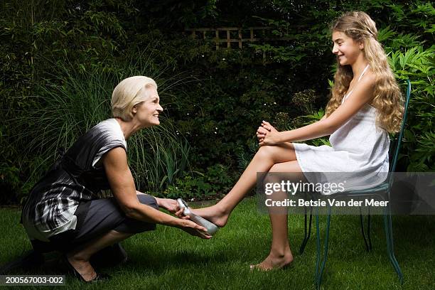 grandma putting silver shoe on granddaughter's (10-11) foot in garden - old cinderella stock pictures, royalty-free photos & images