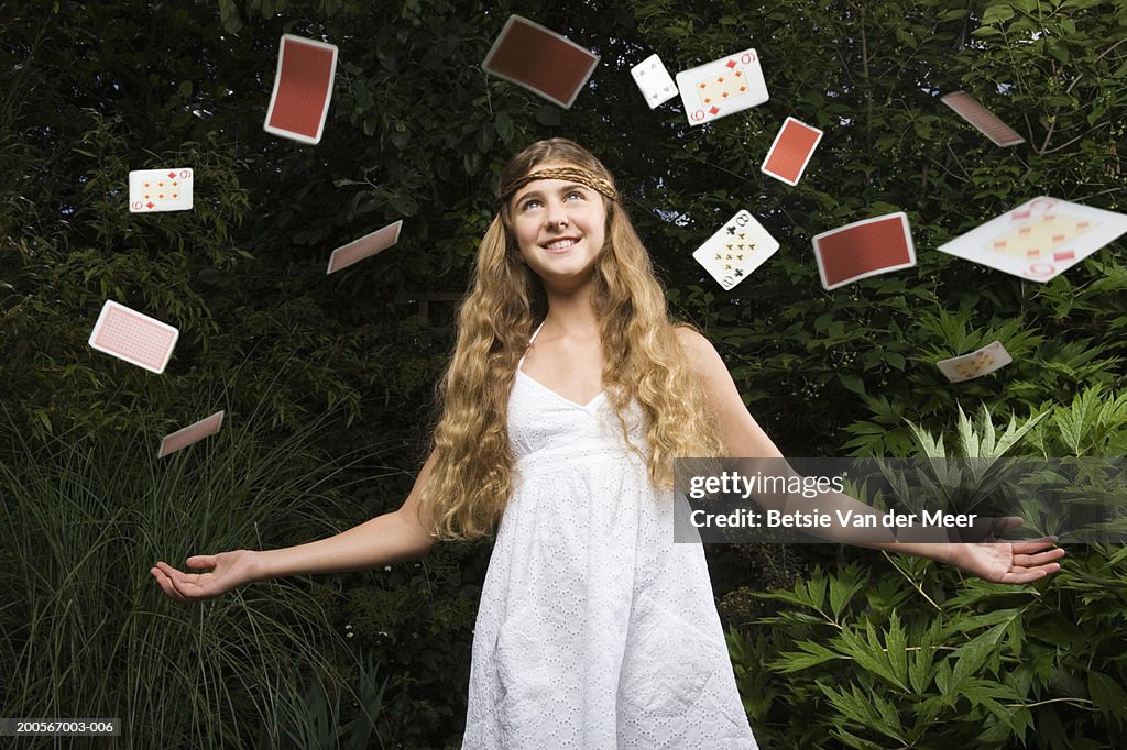 Girl (10-11) throwing playing cards in air, in garden, low angle view