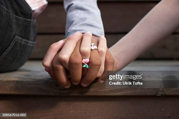 close-up of clasped hands of two girls (12-13) wearing cherry rings - holding hands close up stock-fotos und bilder