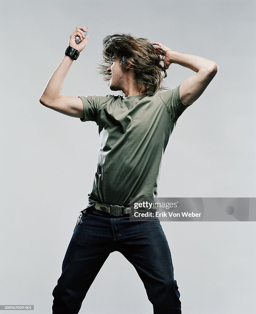 Young man standing with legs apart, holding up mobile phone and shaking head, front view