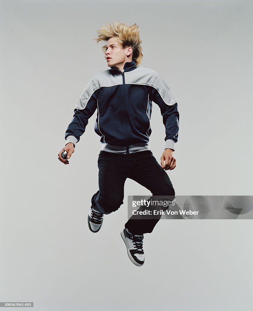 Young man jumping in mid-air, holding mobile phone