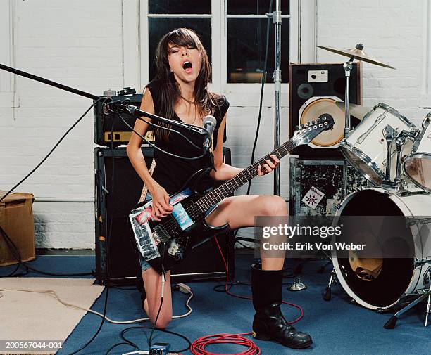 young woman kneeling on one knee playing guitar and singing in music studio - rock'n roll stockfoto's en -beelden