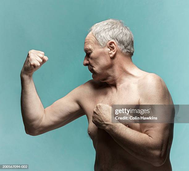 naked senior man flexing biceps against blue background - biceps stock pictures, royalty-free photos & images