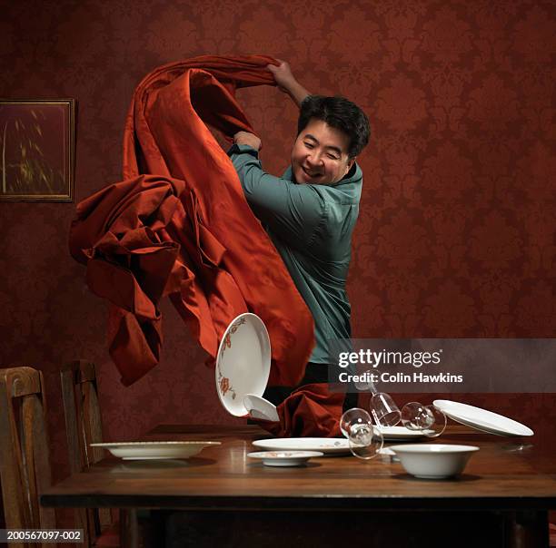 man pulling tablecloth off table, plates and glasses falling over - pull foto e immagini stock