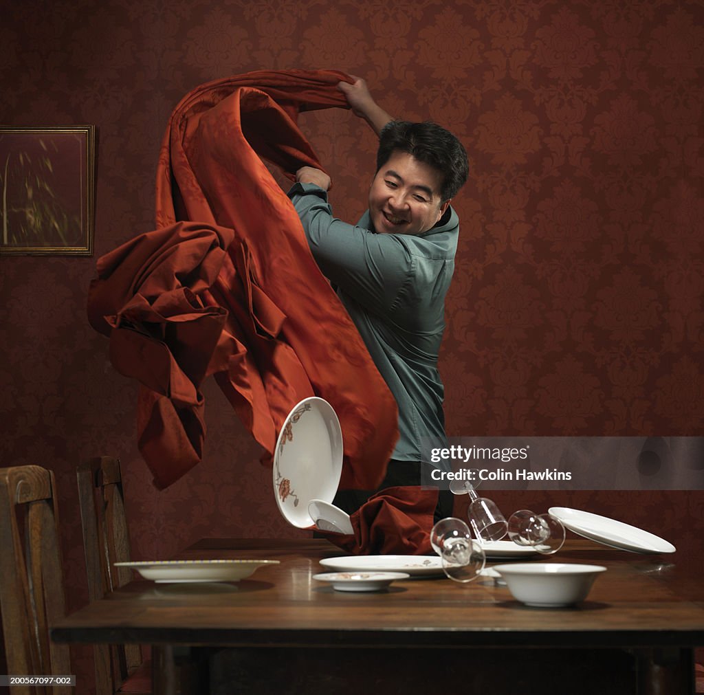 Man pulling tablecloth off table, plates and glasses falling over