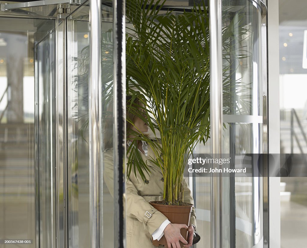 Businesswoman holding potted plant in revolving door