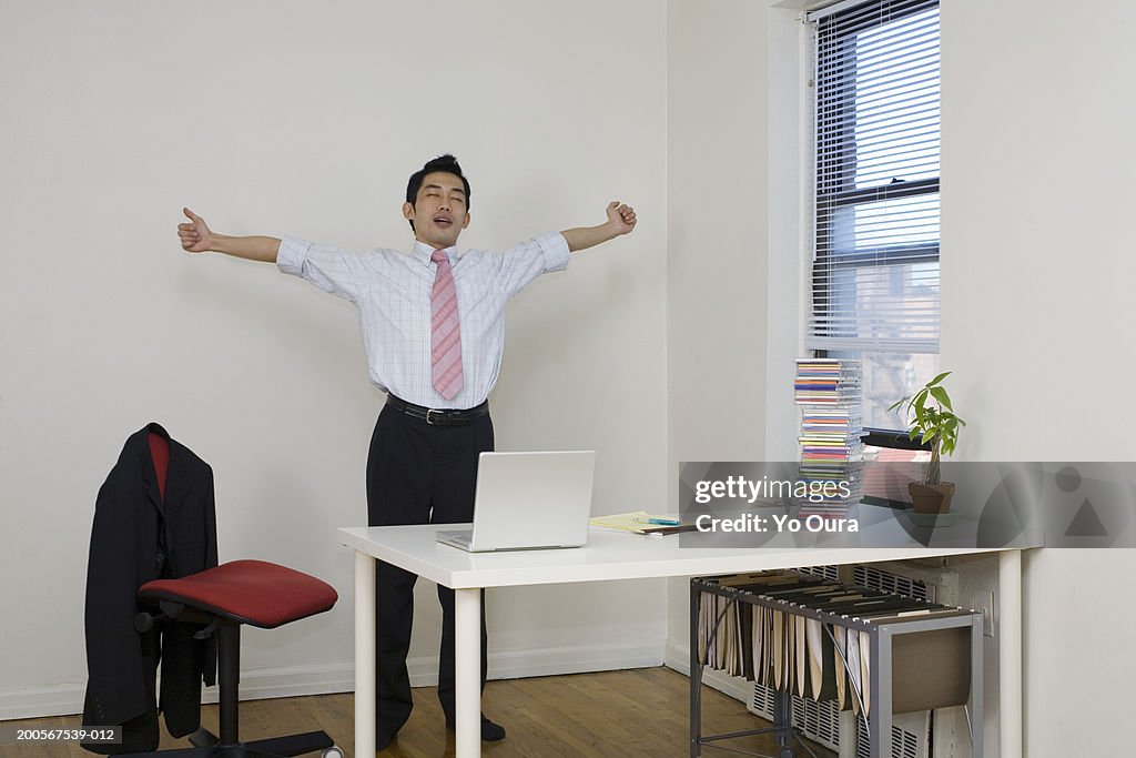 Office worker standing behind desk, stretching