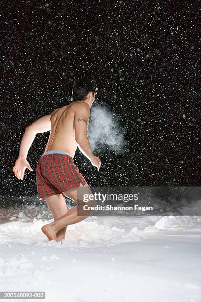 young man wearing boxer shorts running in snow - running shorts foto e immagini stock