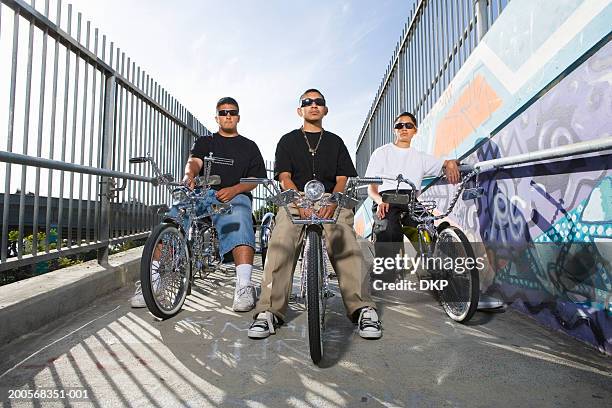 three teenage boys (14-17) on low-rider bicycles with murals on wall - sitting on wall stock-fotos und bilder