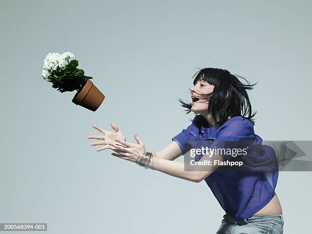 young woman catching pot plant, side view - gefangen stock-fotos und bilder