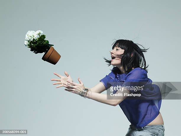 young woman catching pot plant, side view - afferrare foto e immagini stock