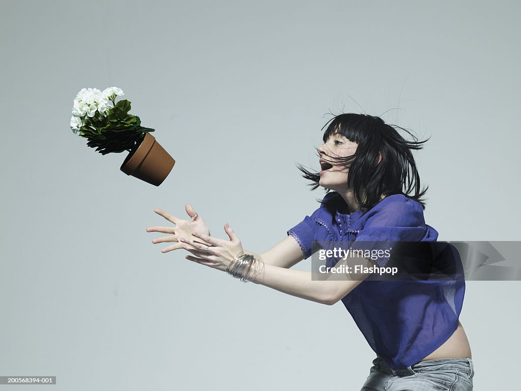 Young woman catching pot plant, side view