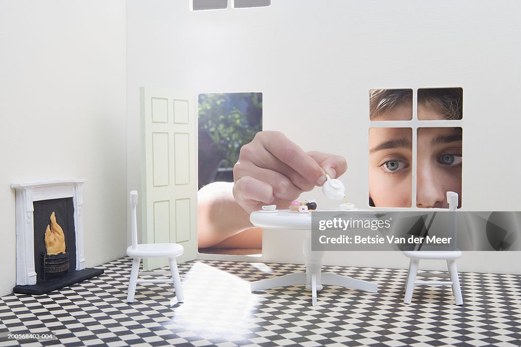 Girl (10-11) peeking through window of dolls house, close-up