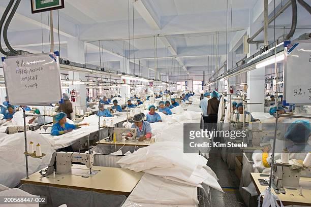 textile workers in long rows at sewing machines making clean suits. - fábrica textil fotografías e imágenes de stock