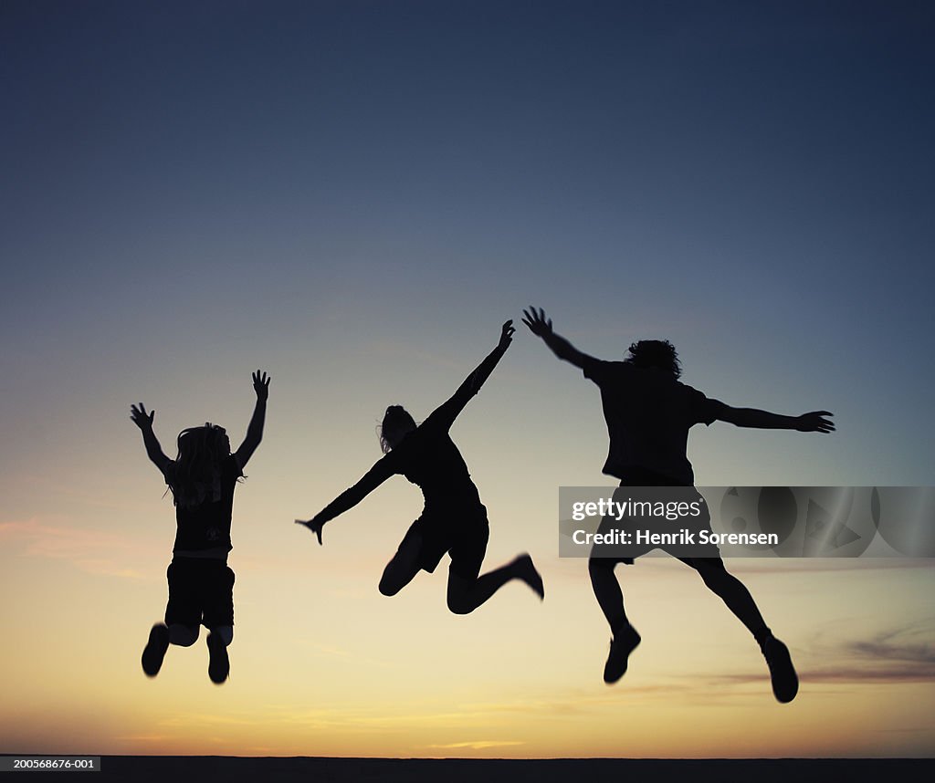 Silhouette of three people jumping in air at sunset