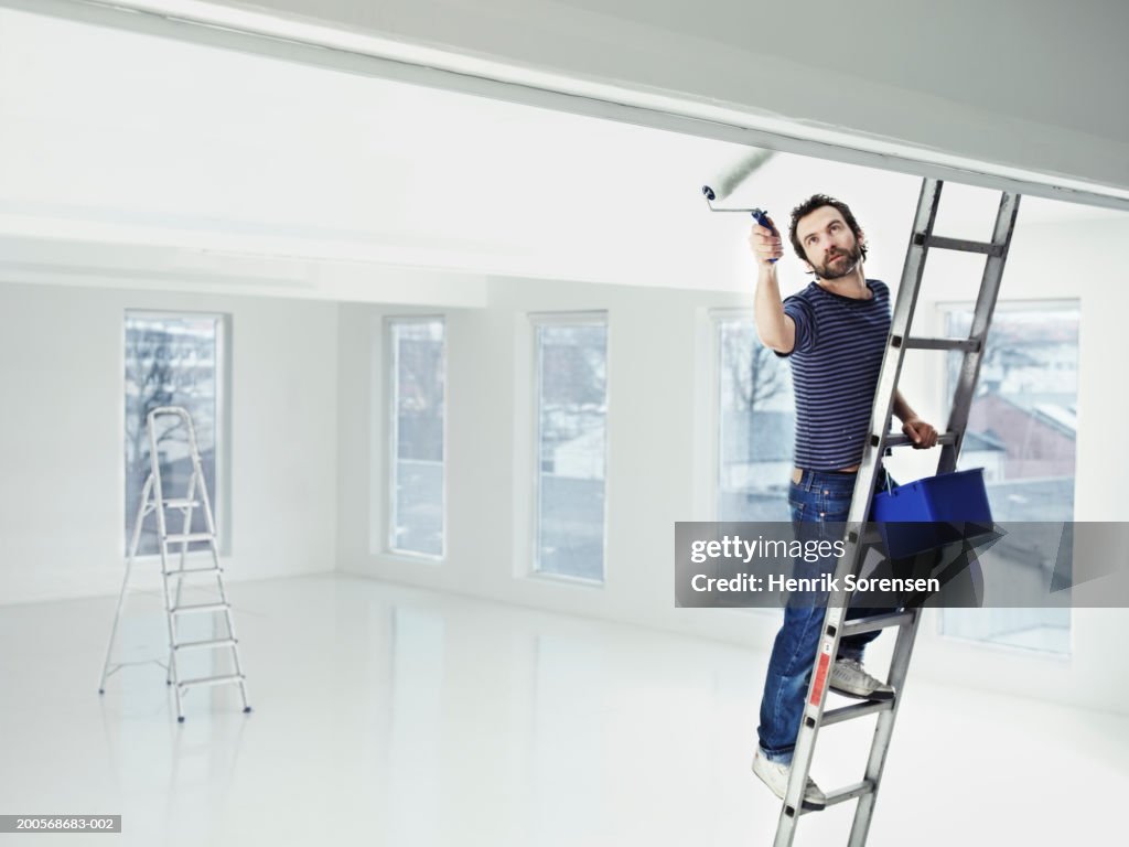 Mid adult man standing on ladder painting apartment