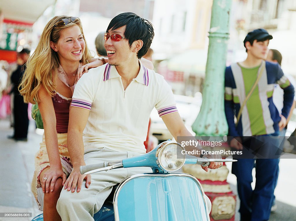 Couple sitting on  scooter on street, smiling