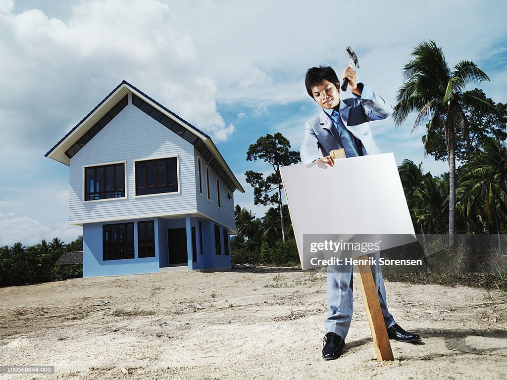 Real estate agent hammering blank sign into ground in front of house