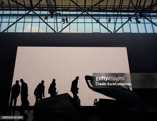 silhouettes of people looking at car displayed at car show - autoshow stockfoto's en -beelden