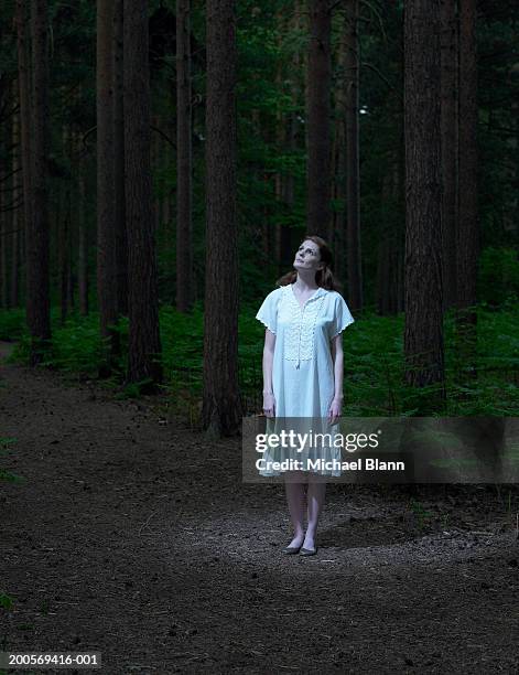 young woman standing in forest, looking up - negligée stock-fotos und bilder