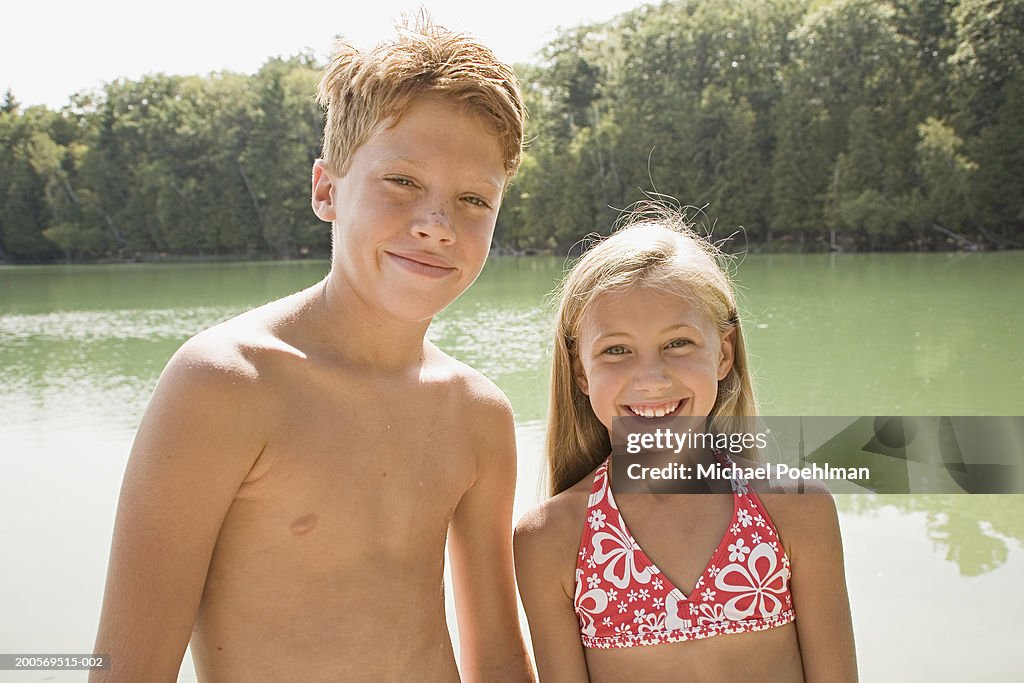 Boy (10-11) and girl (8-9) standing besides lake, smiling, portrait