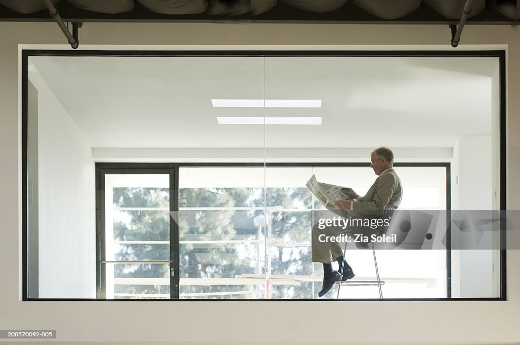 Businessman reading newspaper at empty office, side view