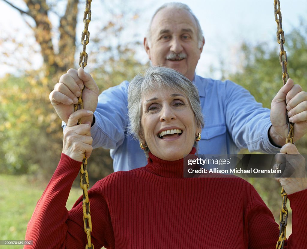 Senior man pushing senior woman on garden swing, smiling, portrait