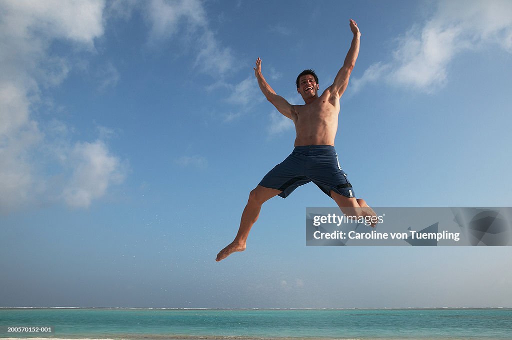 Man jumping on beach, arms up