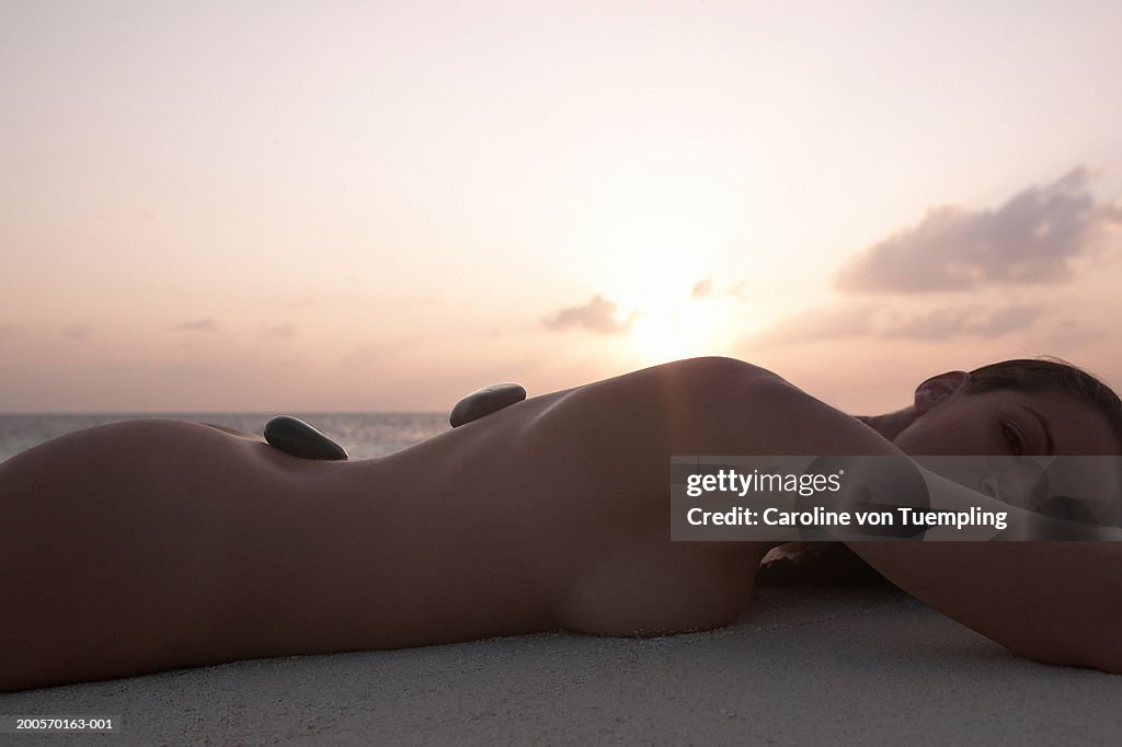 Young woman having lastone therapy on beach, side view