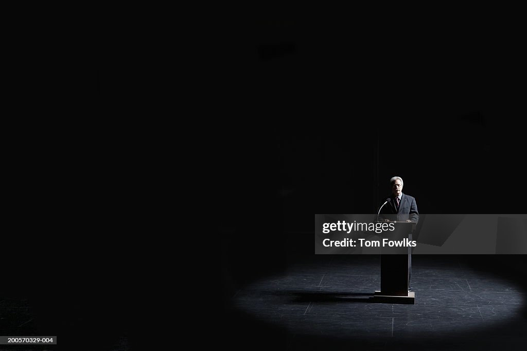 Businessman standing at podium illuminated by spotlight, elevated view