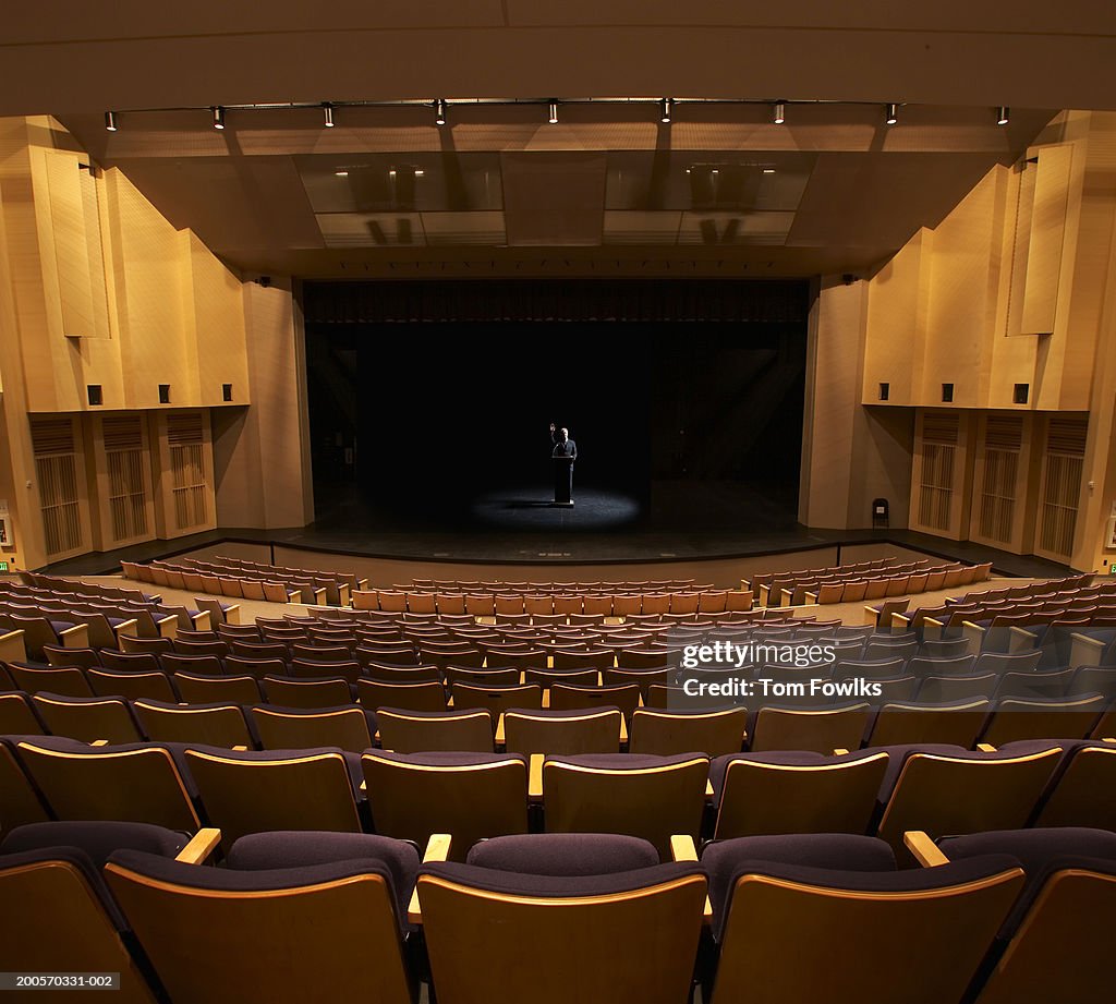 Speaker standing at podium in empty auditorium, elevated view