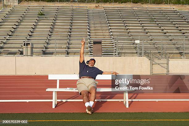 coach sitting on bench on sidelines, holding one finger in air - subs bench fotografías e imágenes de stock