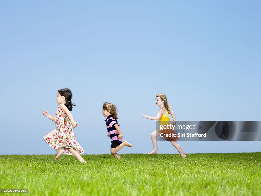 Three children (3-4) running on lawn, side view