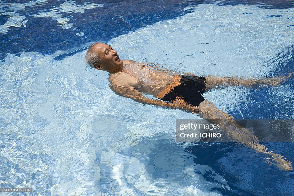 Senior man floating on back in swimming pool, elevated view