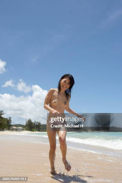 young woman running on beach, smiling, low angle view - portrait beach stockfoto's en -beelden