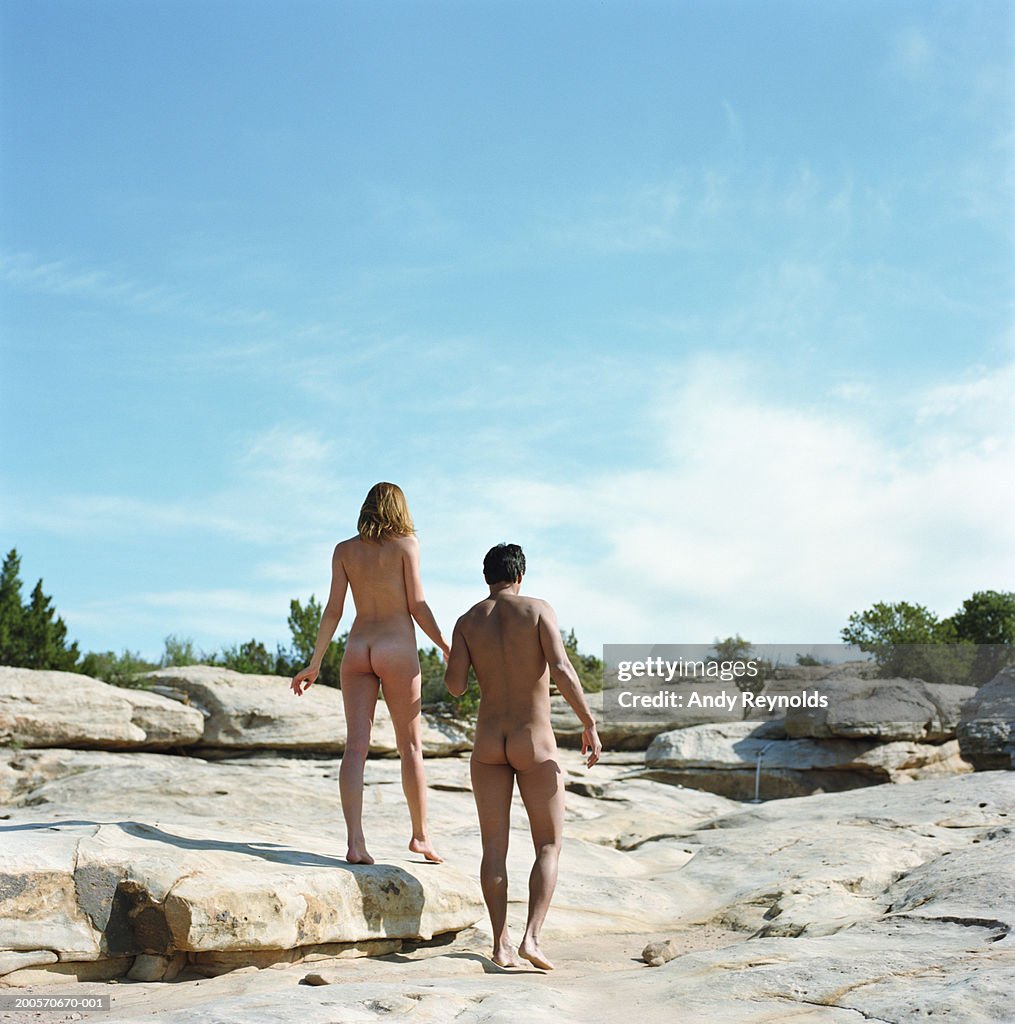 Naked young man and woman walking across rocks in desert, rear view