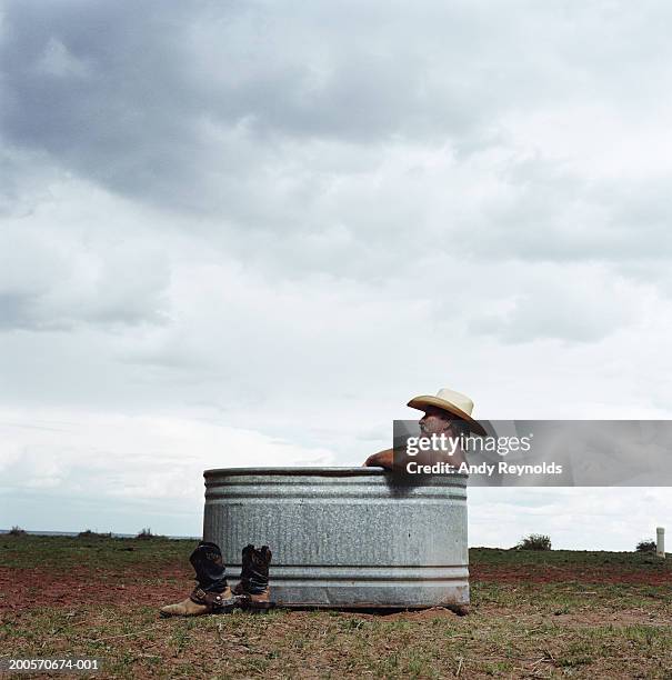 senior man soaking in metal tub in desert, side view - washing tub stockfoto's en -beelden