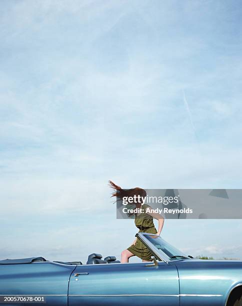 young woman standing in convertible, hair blowing in wind, side view - old car side view stock pictures, royalty-free photos & images