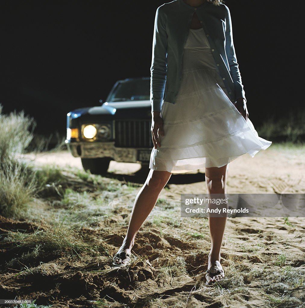 Woman standing in front of car in desert at night, low section