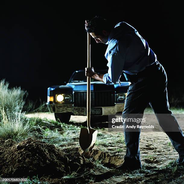 young man digging hole in front of car in desert at night, side view - pala-parte-de-un-vehículo fotografías e imágenes de stock