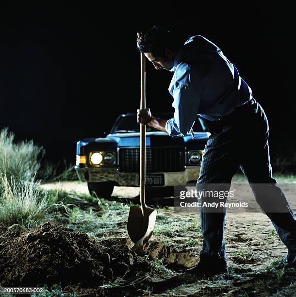 young man digging hole in front of car in desert at night, side view - desertman stock pictures, royalty-free photos & images
