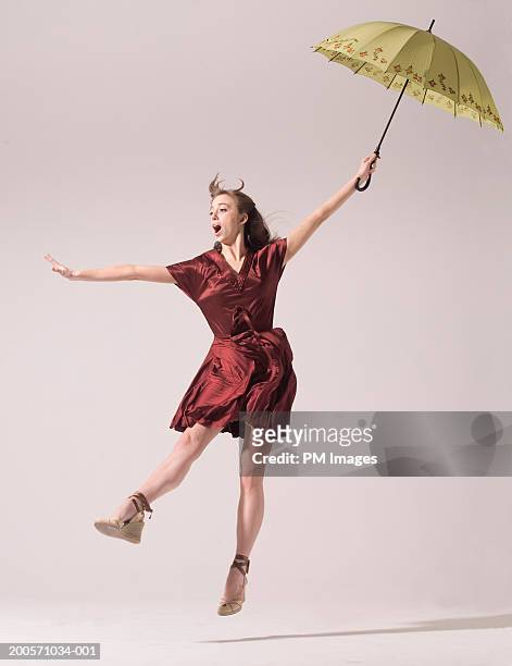 young woman holding umbrella and blowing in wind - holding umbrella stock pictures, royalty-free photos & images